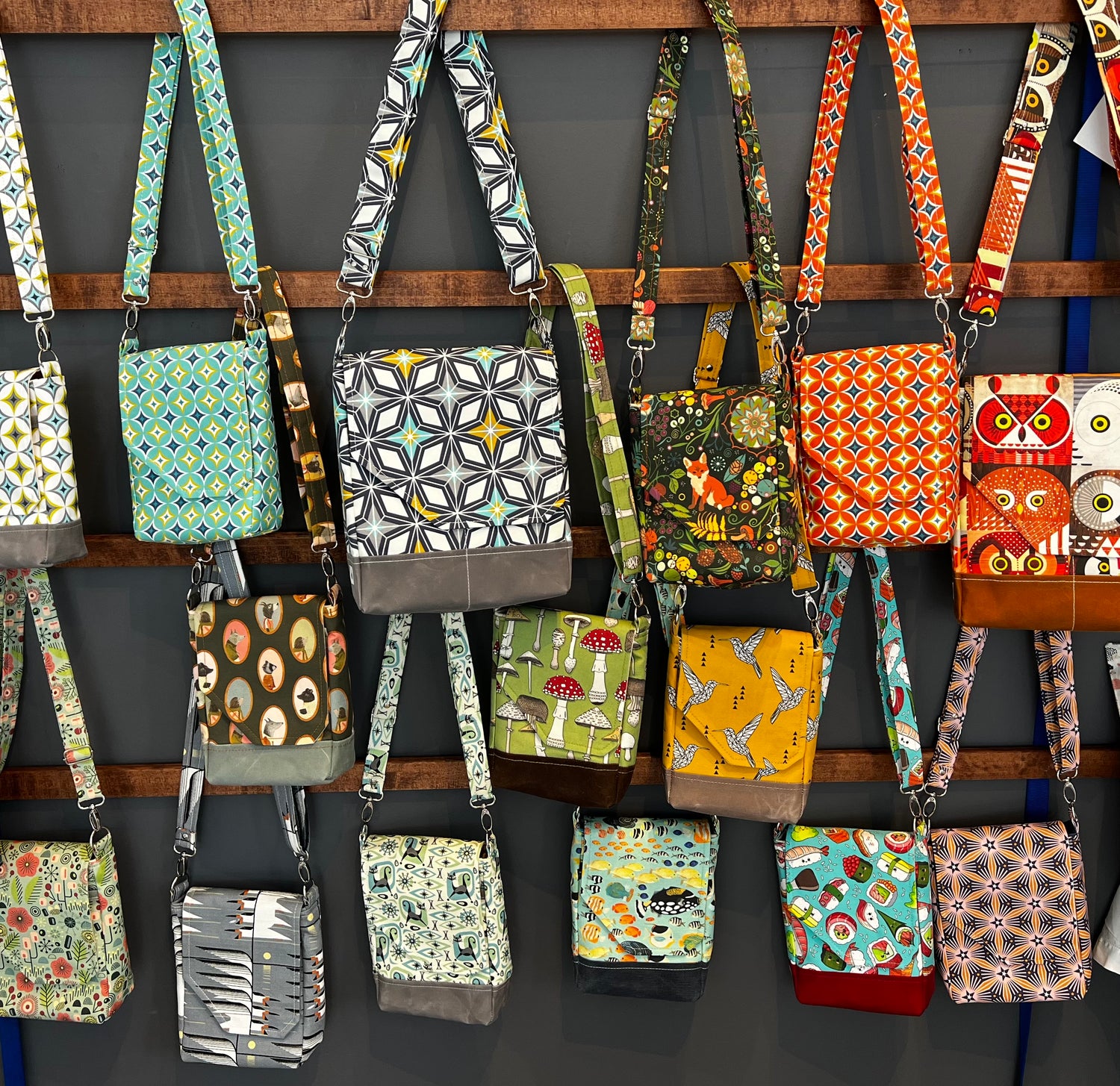 Colorful fabric purses hanging on a display next to a gray wall